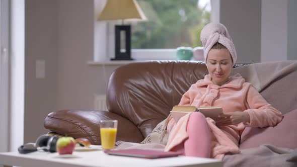 Portrait of Young Relaxed Woman in Bathrobe and Hair Towel Reading Book Enjoying Hobby on Weekend