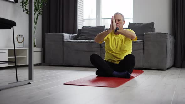 Serious Young Man Meditating at Home Moving Hands in Namaste on Yoga Mat