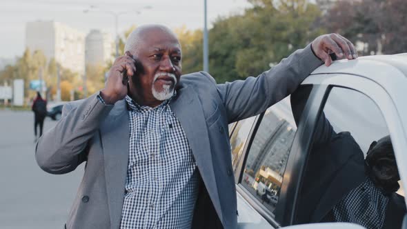 Old African American Man Stands Near Automobile Communicates on Telephone in Street Parking Simple