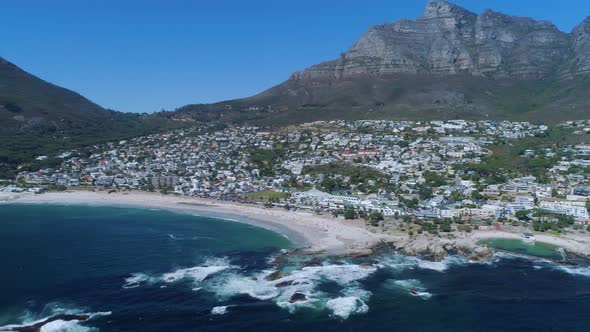 Drone flying backwards, revealing popular Camp's Bay beach and Table Mountain in background