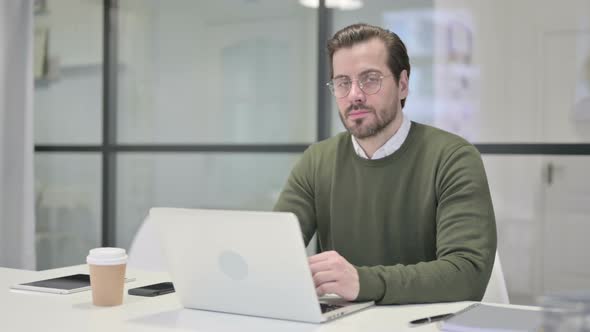 Young Businessman Looking at Camera While Using Laptop in Office