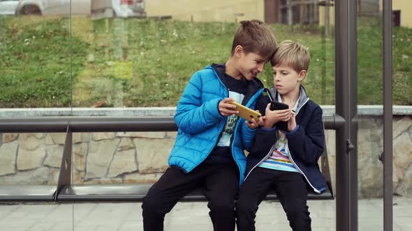 Two Boys Are Sitting At The Bus Stop.