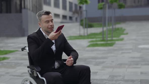 Crop View of Positive Disabled Man in Formal Suit Dictating Voice Message and Sending Outdoors