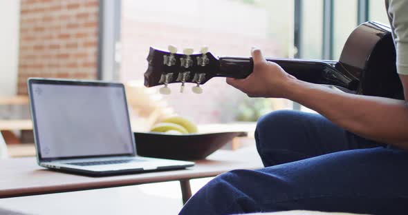 African american man plays guitar and singing, using laptop at home