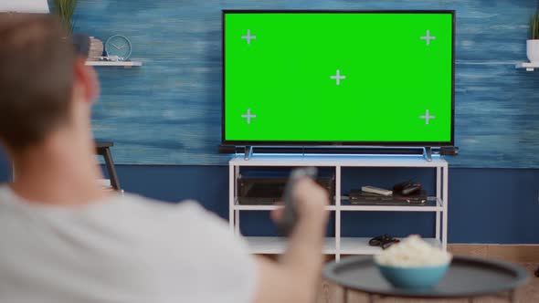 Over Shoulder View of Man Switching Channels While Looking at Green Screen on Tv and Sitting on Sofa