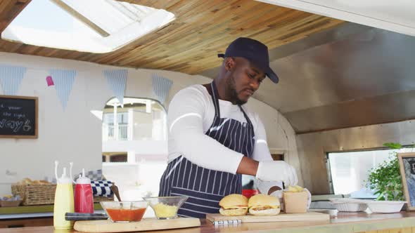 Portrait of african american man wearing apron smiling while preparing burgers in the food truck