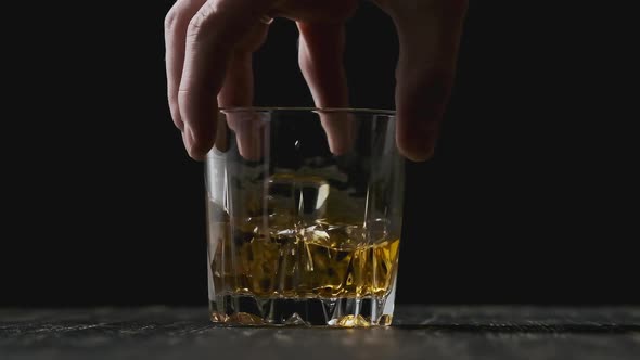 Hand Holds Glass with Golden Whisky. Whiskey with Ice Cubes Rotating in Glass.