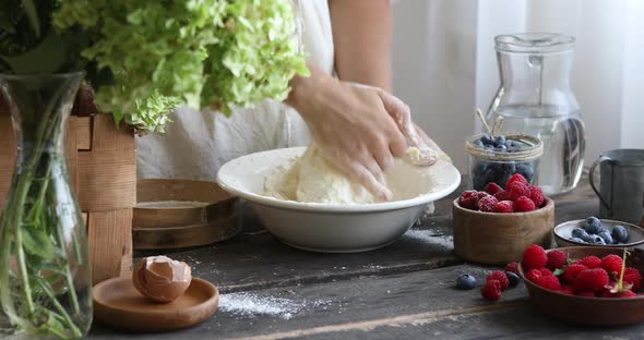 The woman kneads the dough with her hands. Female hands and raw dough on a wooden background.