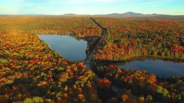 Aerial Footage of Log truck traveling down road between to reflective ponds in autumn colors