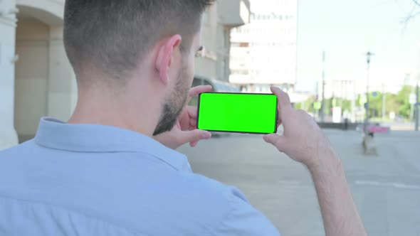 Young Man Watching Smartphone with Green Screen Outdoor