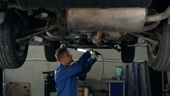 Car Mechanic Examining Car Suspension of Lifted Automobile at Repair Service Station with Light