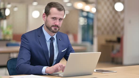 Businessman with Laptop Smiling at Camera in Office