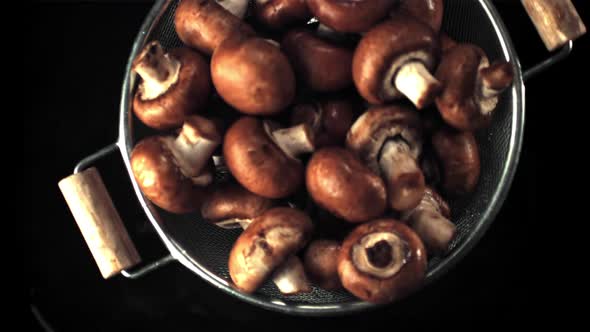 Super Slow Motion of the Colander with Mushrooms Falls on the Water with Splashes