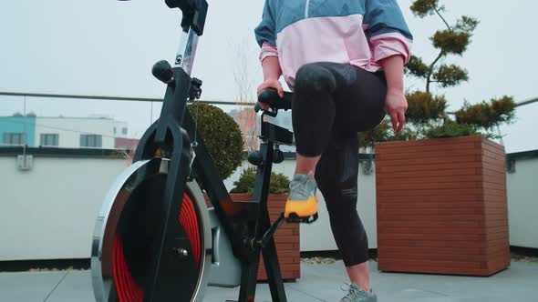 Athletic Girl Performing Aerobic Riding Training Exercises on Cycling Stationary Bike on House Roof