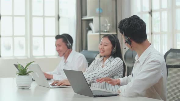Successful Of Three Asian Call Centre Agents Wearing Headsets With Computers At The Office