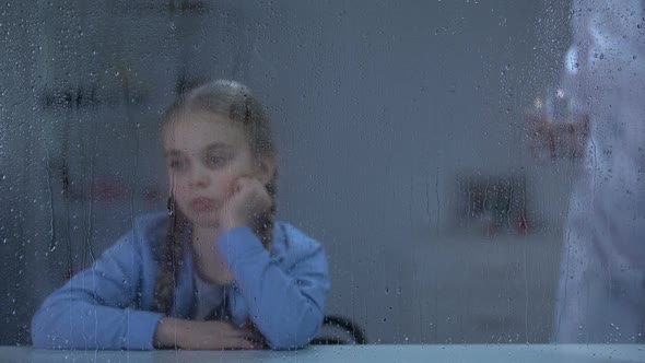 Nurse Bringing Water and Pills to Sick Little Girl Looking Through Rainy Window