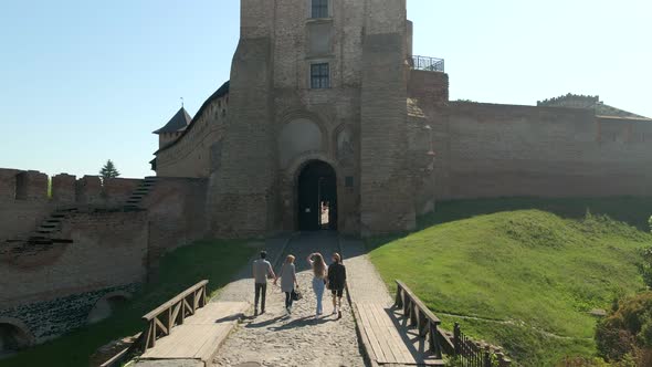 Drone Flies Over Group of Young Friends Walking to Small Medieval Castle in Small European City at