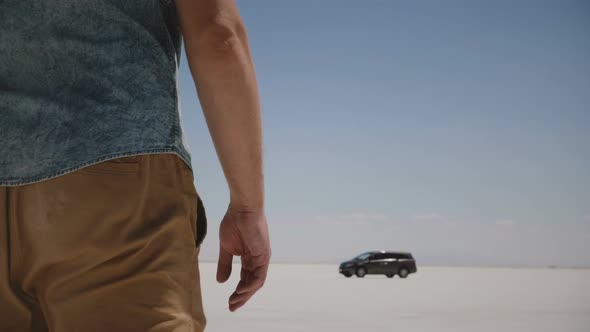 Close-up Camera Follows Young Relaxed Man in Casual Clothes Walking Towards Car in the Middle