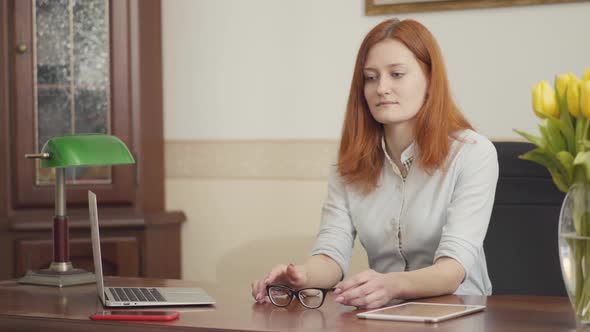 Cute Red-haired Woman Psychologist Sitting at the Table Waiting for a Patient in the Office