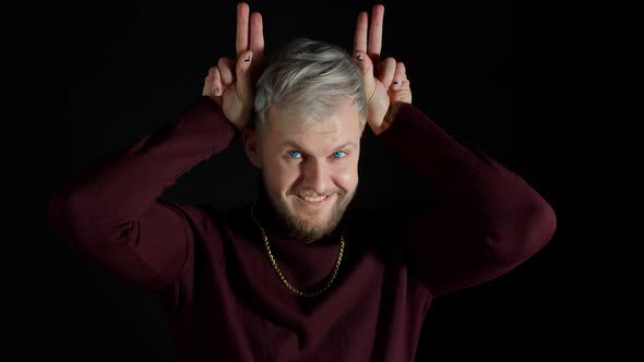 Funny Joyful Man in Stylish Blouse Making Bunny Ears Hand Gesture Over Head on Black Background