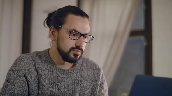 A Young Handsome Man in Glasses Works on a Laptop