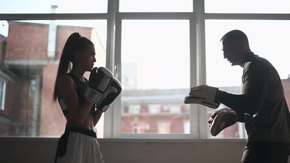 A Young Girl Conducts Kickboxing Training and Practices Paw Strikes with a Professional Boxer