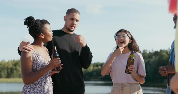 Couple in Love is Standing Near Lake with Their Friends They are Talking Woman is Explaining Story