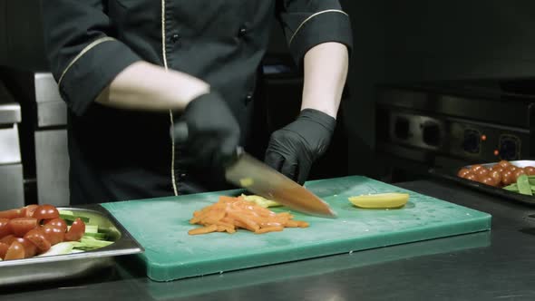 Cook's Hands in Black Gloves Slicing Yellow Paprika