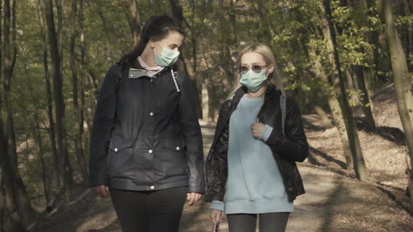 Portrait of Blond and Brunette Women in Face Masks Walking in Park on Sunny Spring Day. Young