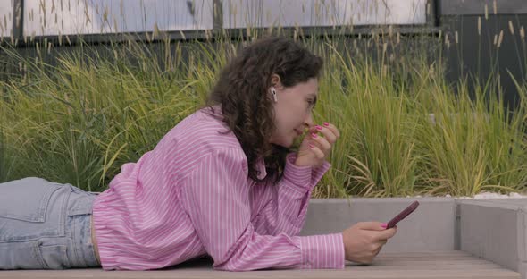 Joyful woman wearing pink shirt using a mobile phone, typing text messages, listening music