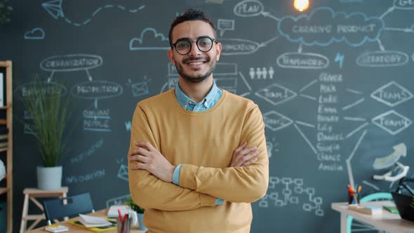 Portrait of Good-looking Arab Businessman Standing in Open Space Office with Arms Crossed Smiling