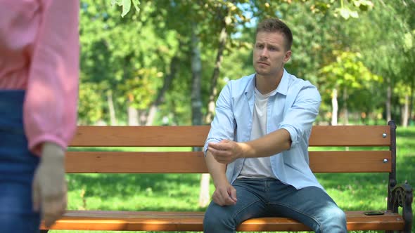 Woman Leaving Upset Boyfriend Alone on Bench in Park, Walking Away, Break-Up