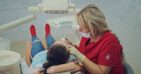 Pretty Woman Dentist Treats a Tooth to a Young Girl Works with the Tool