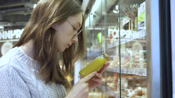 A Young Female Customer Reads the Composition of the Drink on the Juice Bottle