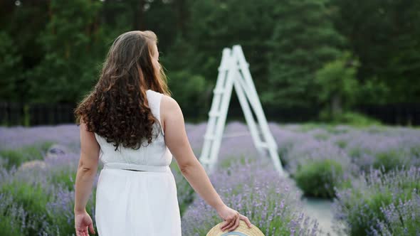 Portrait of Attractive Joyful Brunette Woman Walking Down the Lavander Field on White Dress Holding