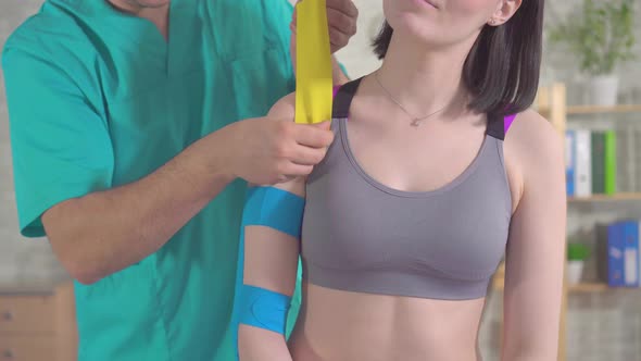 Physical Therapist in Uniform Sticks Kinesiotape on Patient's Shoulder