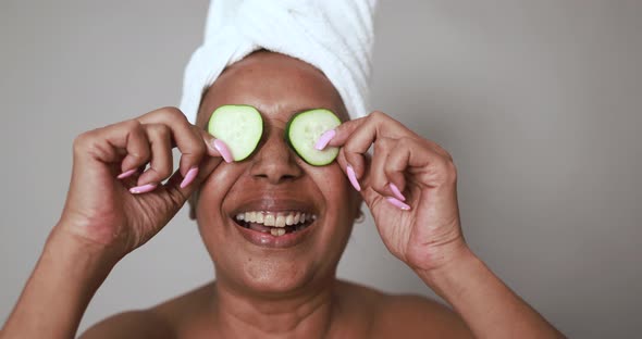 African senior woman holding cucumbers on her eyes - Beauty treatment and body care concept