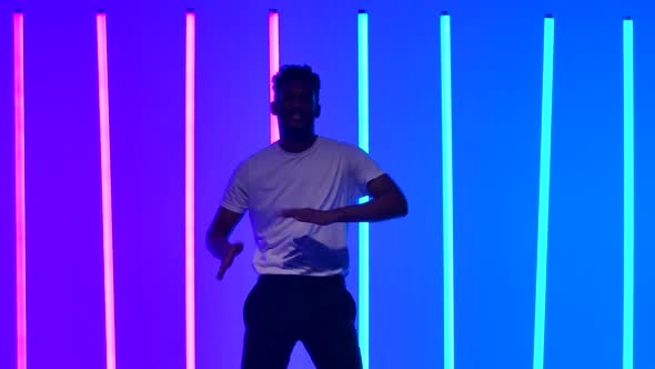 Flexible African American Man Dancing in the Studio Against the Backdrop of Multicolored Neon Lights