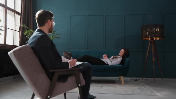 Young Woman Visiting Male Psychologist Lying on the Comfortable Couch During Psychological Session