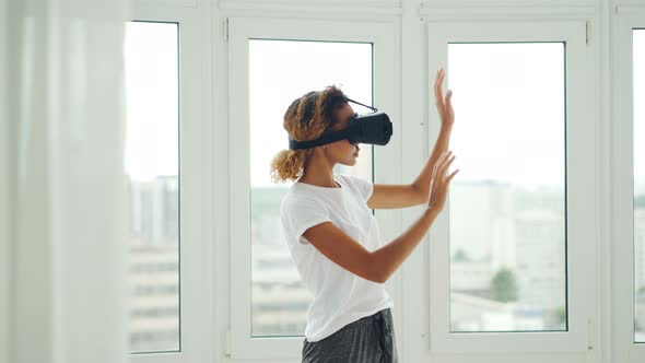 African American Girl in Casual Clothes Is Using Virtual Reality Glasses and Gesturing While