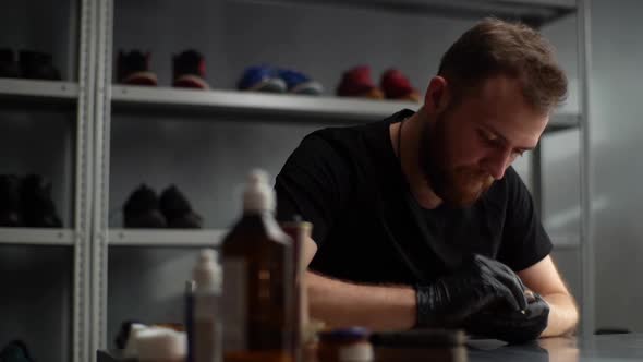 Tracking shot of shoemaker in black latex gloves cleaning old light brown leather shoes with rag.