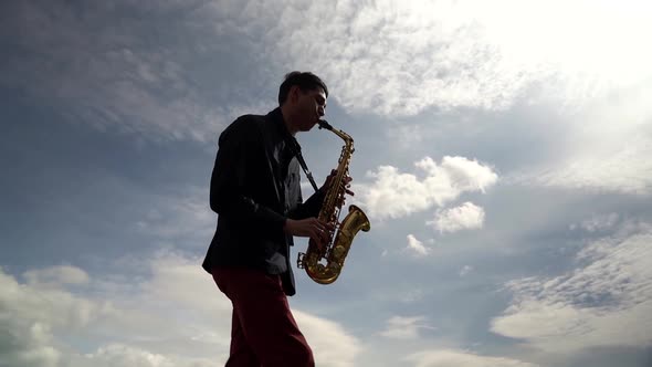 a Man in a Dark Shirt Plays the Saxophone Emotionally Against a Sky with Clouds. Bottom View