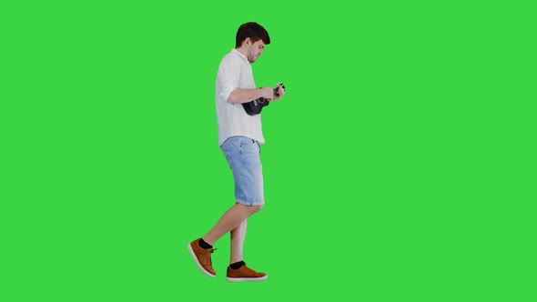 Young Man Playing Ukulele While Walking on a Green Screen, Chroma Key.