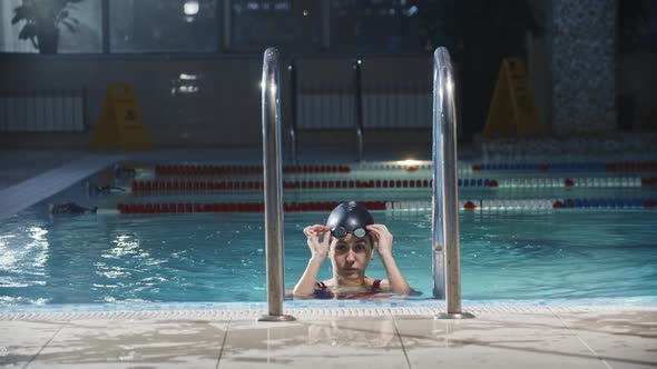 Swimming Sports  Young Woman Swimmer Comes Up From the Pool on the Ladder