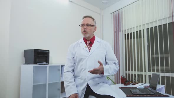 Smiling doctor sitting at his desk in his office. Doctor is working in his medical office