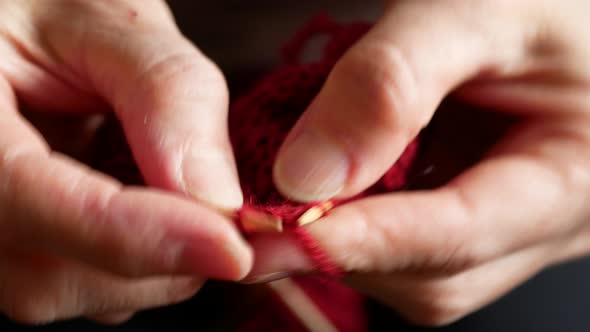 Woman is knitting the cold-weather clothing using the burgundy yarn with natural fabrics