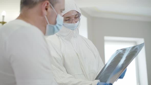 Portrait of Professional Female Doctor in Antiviral Suit Explaining Lungs Roentgen To Ill Patient