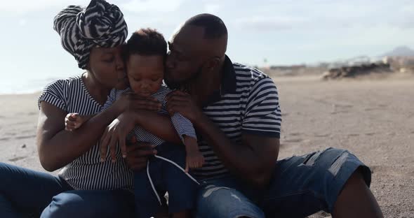 Happy african parents having tender moment on the beach with little son