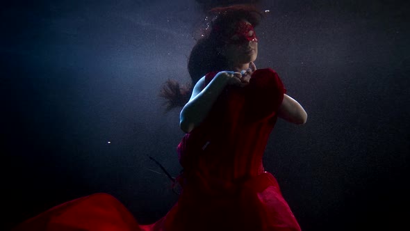 Young Woman with Masquerade Mask on Face Is Swimming Underwater