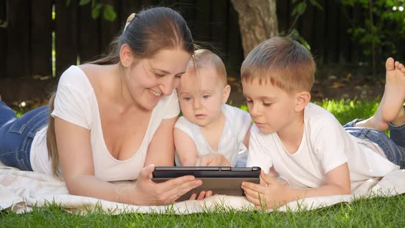Happy Mother with Older and Baby Son Browsing Internet in Park on Tablet Computer